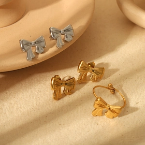 Detail view of 18k gold plated bowknot earrings and ring set on minimalist fabric