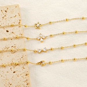 Détail de quatre bracelets dorés avec pendentifs étoile, trèfle, nœud et zircon