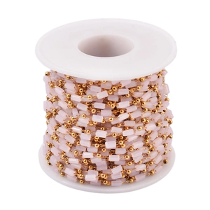 Macro view of gold stainless steel chain with pink stone beads on a white spool