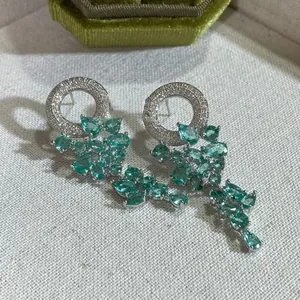 Gros plan de boucles d'oreilles argentées avec cristaux goutte vert émeraude sur tissu blanc
