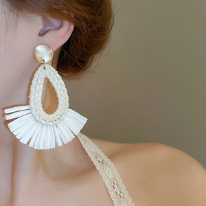 Détail de boucles d'oreilles bohèmes faites main en raphia portées par un mannequin