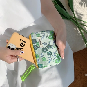 Mini floral canvas storage bag with yellow zipper and neon green drawstring held by hand