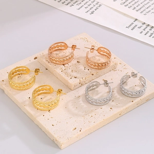 Vue détaillée de boucles d'oreilles créoles en or, argent et or rose sur support en pierre