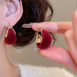 Detail of dark red velvet U-shape earrings with gold metal clasp on model and hand