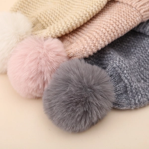 Detailed view of soft knit texture and fluffy faux fur pom-poms on baby winter hats