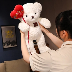 Close-up of white plush teddy bear holding a red heart with Happily Ever After embroidery