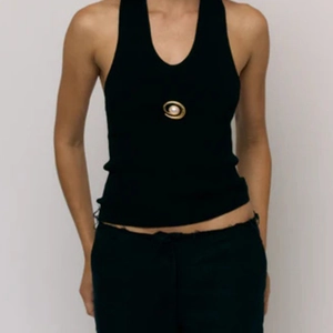 Detail of a black ribbed halter top featuring a gold spiral pearl brooch ornament