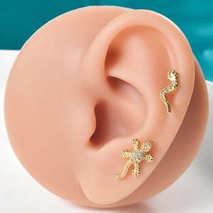 Close-up of gold snake and lizard earrings with rhinestones on a silicone ear model