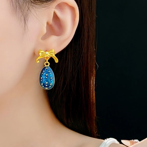 Dettaglio di orecchini a fiocco vintage con pendenti in smalto blu indossati da modella