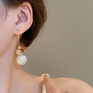 Detail of gold metal disc earrings with white pearl pendants worn on a model's ear