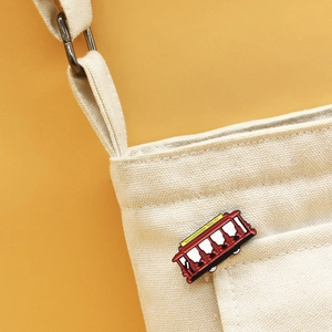 Detail of Neighborhood Trolley enamel pin on a canvas bag against a warm yellow background