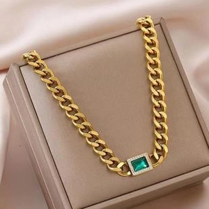 Macro view of golden Cuban link necklace with green emerald-cut stone in a gift box