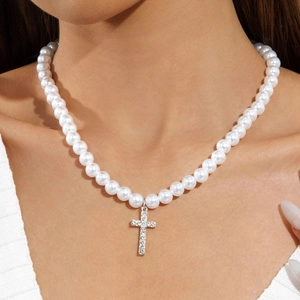 Close-up of a pearl necklace with a silver cross pendant inlaid with sparkling crystals