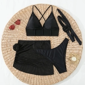 Flachbild eines schwarzen 3-teiligen Bikinis mit Netzrock und 3D-Blumen auf Strohmatte
