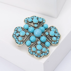 Detail of vintage bronze four-leaf clover brooch with turquoise stones on white stand