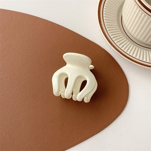 Detailed view of a cream-colored matte hair claw clip on a brown leather pad