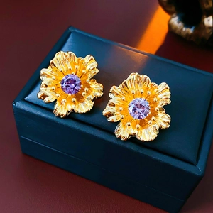Close-up of golden flower earrings with purple zircon stone on a jewelry box