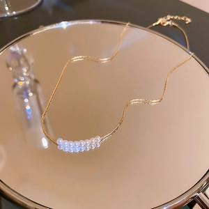 Detailed close-up of a minimalist gold pearl necklace on a reflective mirror tray