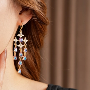 Close-up of gold cross earrings with purple gems and drop pendants on a model