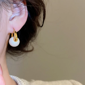 Detail of gold-plated hoop earring featuring a textured white spherical pendant on a model