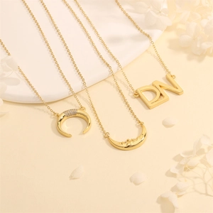 Detail of 18k gold moon and letter DN pendants with zircon inlays on a white tray