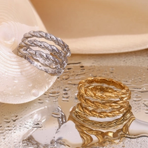 Close-up of gold and silver twisted rope rings on a reflective surface with water drops