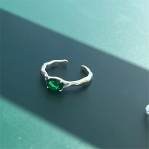 Macro shot of 925 sterling silver ring with oval green emerald and wavy liquid metal band