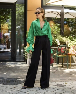 Close-up of green long sleeve shirt with flare cuffs and black wide-leg trousers detail