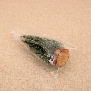 Close-up of a mini snowy pine Christmas tree with a natural round wood base in packaging