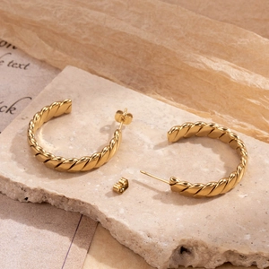 Luxurious gold C-shaped braided rope texture hoop earrings displayed on stone