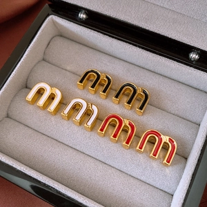 Detailed macro view of letter M enamel earrings in gold, black, white, and red finishes
