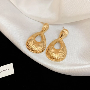 Macro detail of golden teardrop earrings with intricate radial pleated textures on satin