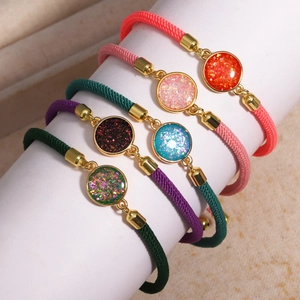 Detail of colorful braided rope bracelets with round golden glitter charms on a stand