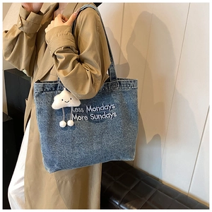 Detail of blue denim tote bag featuring white embroidery and cloud pendant on strap