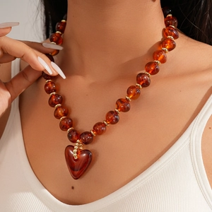 Close-up of amber acrylic oval beads and heart pendant necklace worn by a model