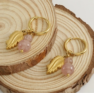 Detail of gold leaf earrings with pink natural stone on rustic wood slices