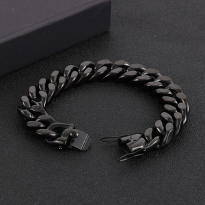 Gros plan d'un bracelet gourmette en acier inoxydable noir avec fermoir dragon sur sable noir