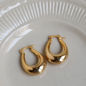Detailed view of polished gold teardrop hoop earrings on a white ceramic tray