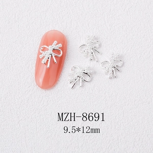 Macro shot of silver bow nail charm with white pearls on a pink manicured nail