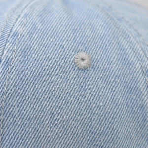 Detail of washed denim baseball cap featuring fine stitching and grey ventilation eyelet