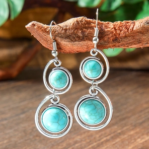 Detail of silver bohemian teardrop earrings with turquoise stones hanging on a wooden branch