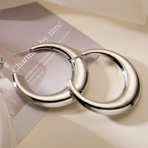 Close-up of chunky silver-plated crescent hoop earrings on a warm cream background
