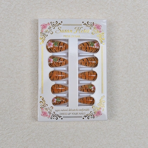 Detail of almond press-on nails featuring tiger stripes and floral 3D accents in box