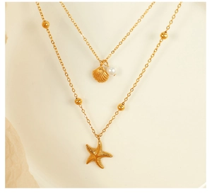 Macro detail of gold layered necklace with starfish shell charms and white pearl