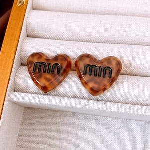Close-up of tortoise shell heart stud earrings with miu lettering in a jewelry box