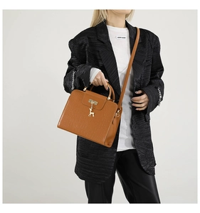 Close-up of brown crocodile texture bag with gold deer pendant and metal handle ring