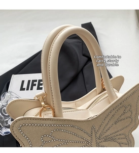 Close-up of beige leather tote bag with rhinestone butterfly design and golden hardware