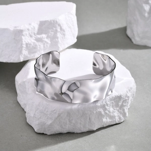 Detail of silver C-shaped open cuff bracelet with a unique wavy texture on white stand