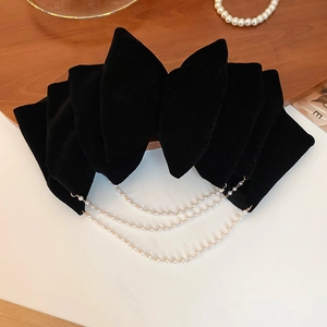 Detail of a black velvet bow hair clip with triple-layered pearl tassels on wood background