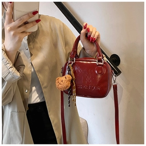 Detail of a dark red patent leather handbag with double handles and a cute plush bear charm